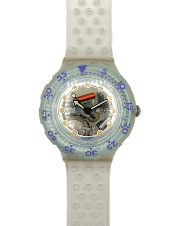 A Swatch wristwatch with a translucent light blue-green bezel, a white textured silicone strap, and a visible mechanical movement inside the clear dial.