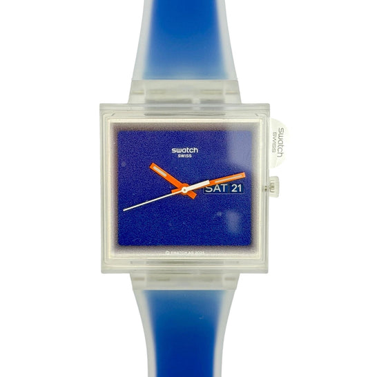 Swatch Swiss wrist watch with a translucent blue silicone strap, a clear square case, and a textured blue dial featuring orange and white hands.
