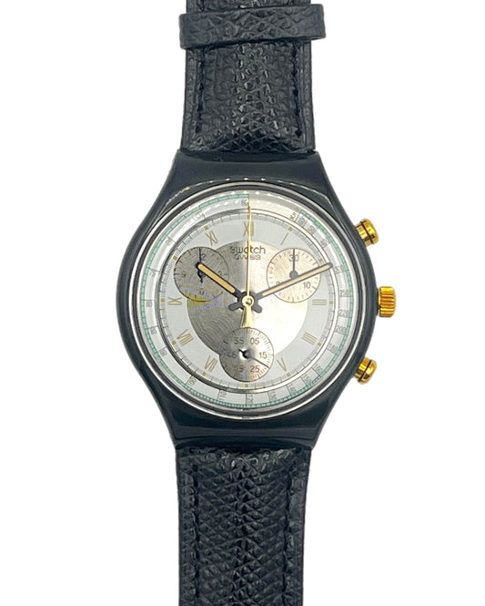 A vintage-style wristwatch with a textured black strap, a dark gunmetal bezel, and a silver dial featuring a heart-shaped cutout design and gold-tone accents.