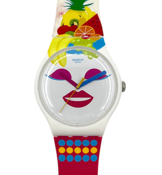 A Swatch wristwatch featuring a colorful fruit and pineapple design on the strap, a white dial with a stylized face made of lips and sunglasses, and a red lower strap with blue and yellow dots.