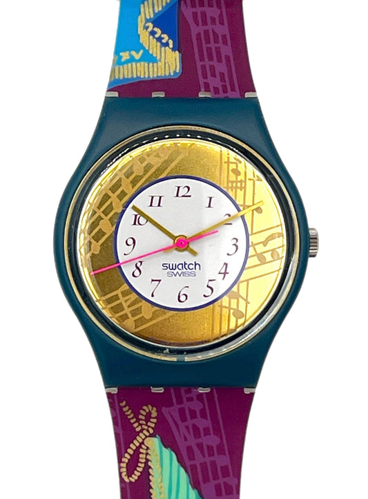 Swatch wristwatch with a colorful patterned strap and a gold-toned bezel, shown on a plain white background.